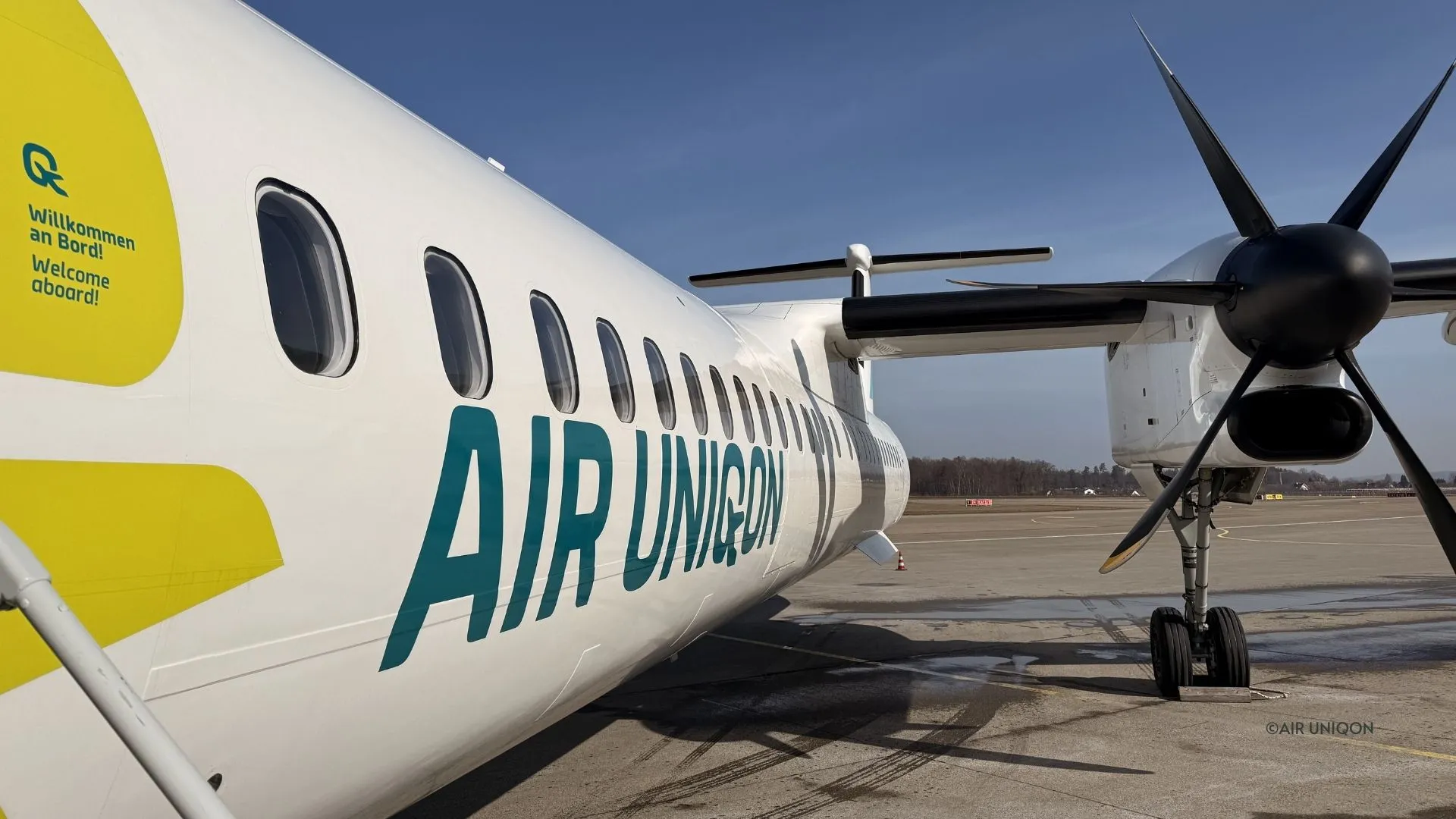AIR UNIQON Schriftzug und Propeller einer Dash 8-400, an der Tür „Willkommen an Bord!“