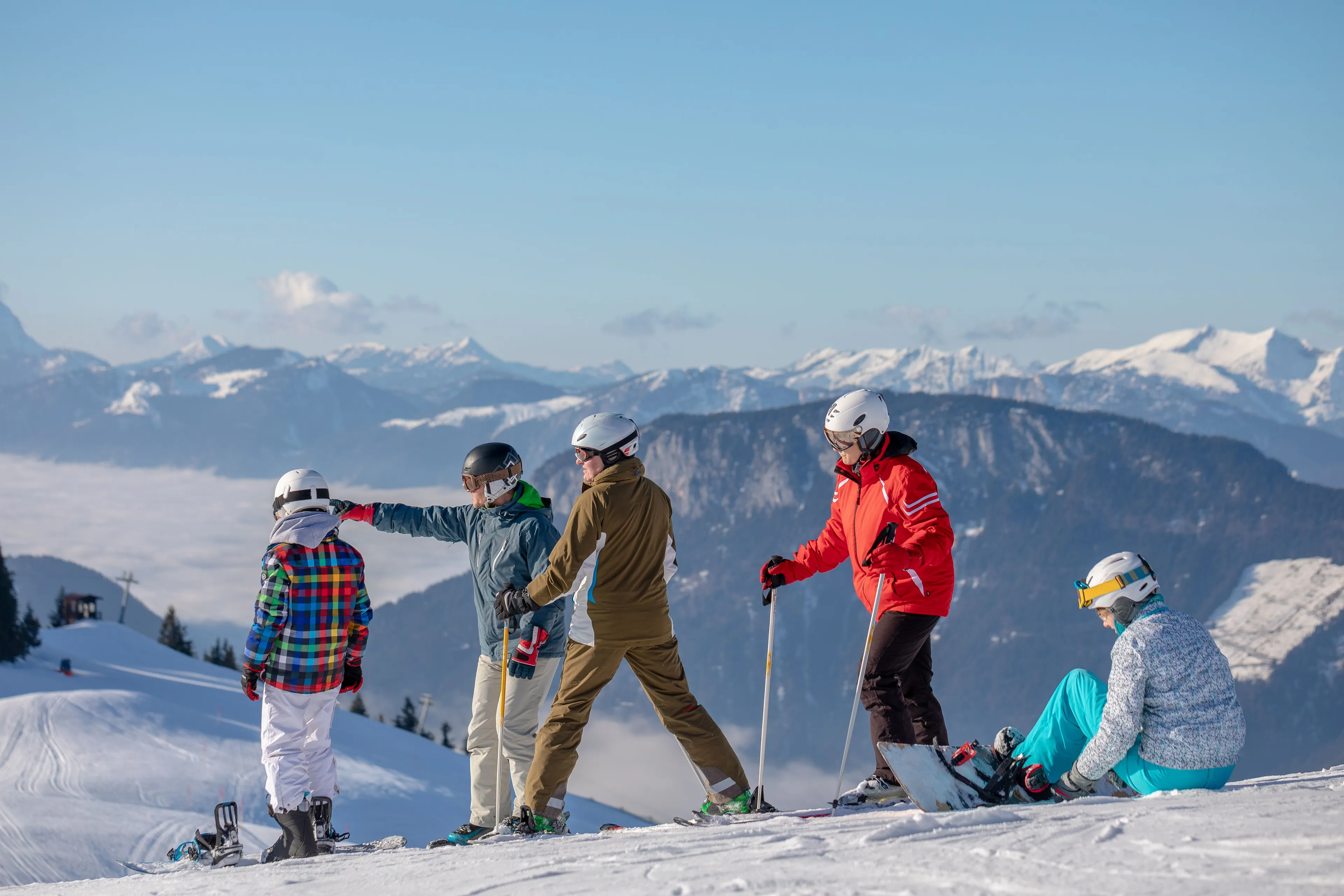 Gruppe von Skifahrern und eine Snowboarderin auf einer Piste mit Bergpanorama